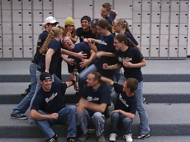 Drumline students piled together laughing on the stairs after rehearsal