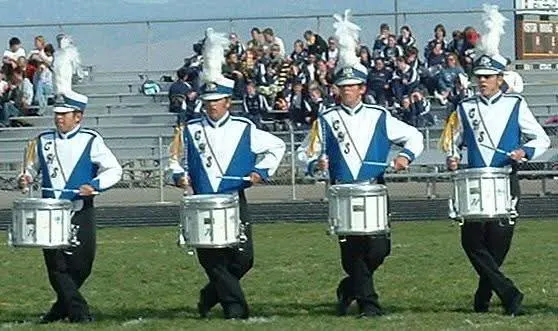 Four marching snare drummers performing in uniform on the field