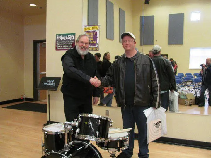 Sam Bowker shaking hands beside a drum kit at an awards event